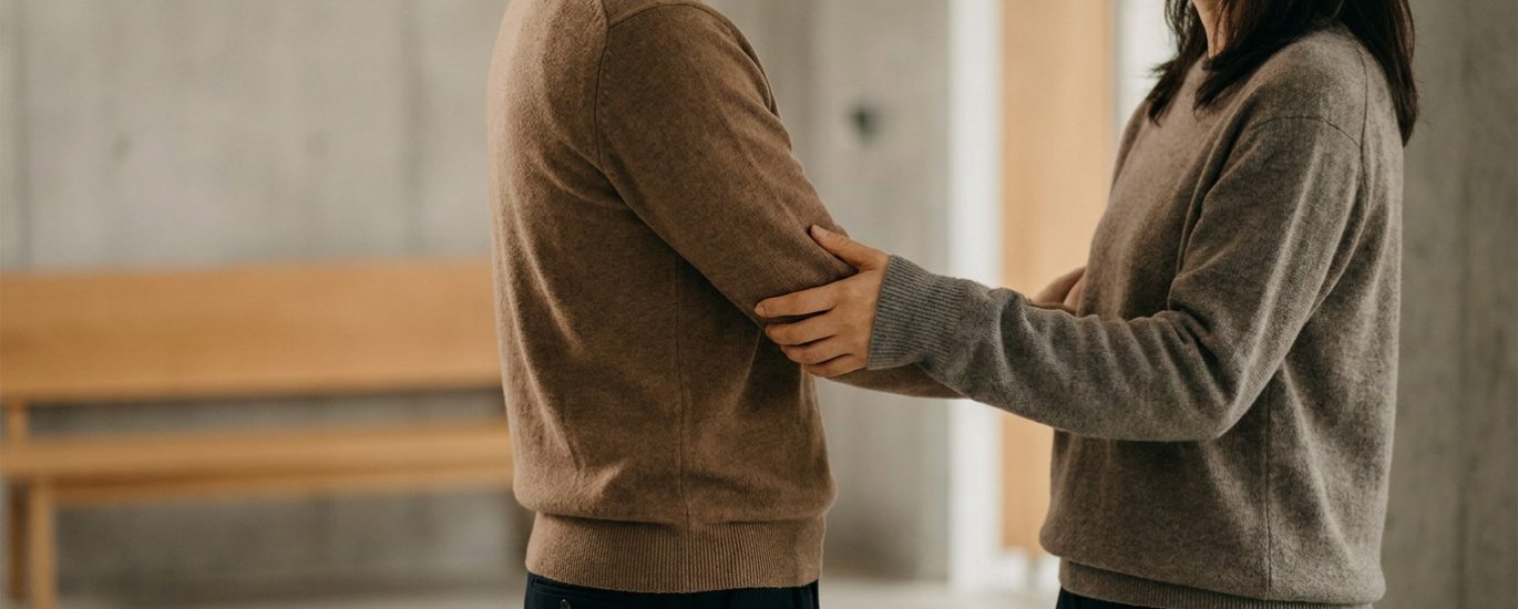 Un homme et une femme se tenant face à face, se tenant doucement le bras dans une interaction intime et respectueuse.