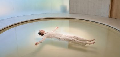 Une personne vêtue de vêtements clairs flotte paisiblement sur le dos au centre d'une piscine circulaire minimaliste.