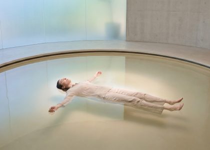 Une personne vêtue de vêtements clairs flotte paisiblement sur le dos au centre d'une piscine circulaire minimaliste.